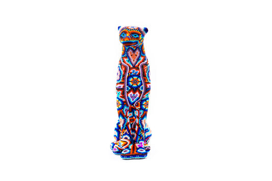 Escultura vertical y estilizada de un guepardo en chaquira, con un patrón de arte Huichol vibrante que muestra múltiples colores como azul, rojo, naranja, y detalles en blanco. La figura tiene una pose recta y majestuosa, con una expresión atenta y ojos detallados.