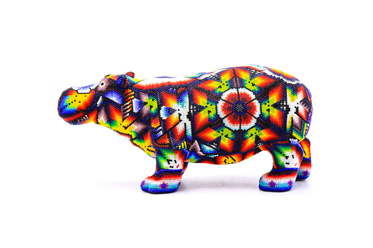 Figura de hipopótamo de artesanía Huichol con decoración de cuentas multicolores sobre fondo blanco, representando la rica cultura Wixarika y su arte vibrante