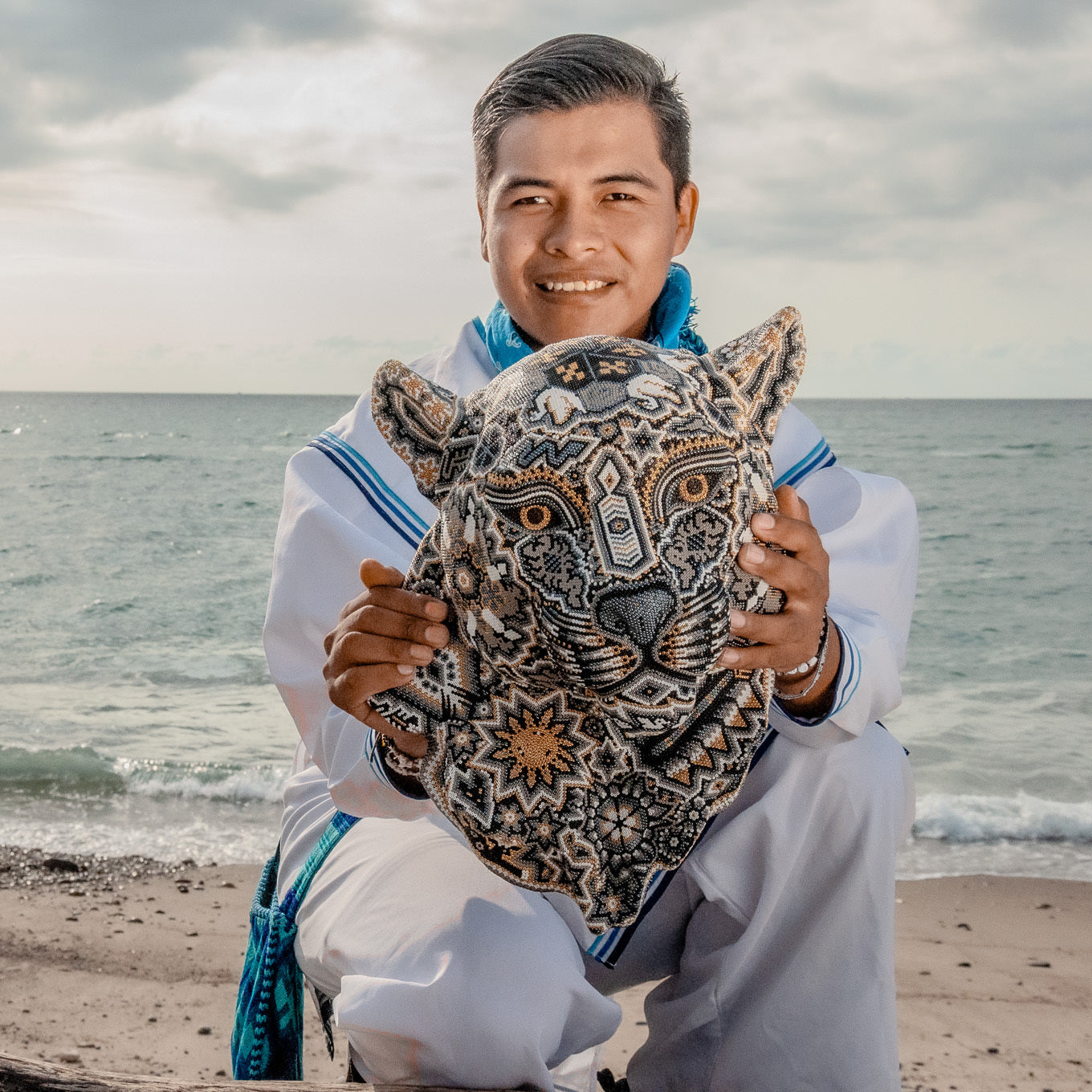Artesano huichol sosteniendo una obra de arte que representa al jaguar con simbolos wixarikas