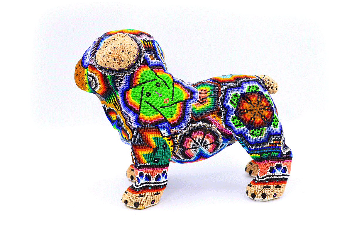 Artesanía wixárika en forma de bulldog bebé, cubierto con un mosaico colorido de chaquira que muestra patrones geométricos y símbolos tradicionales huicholes en una vibrante paleta de colores, resaltando el rostro curioso del cachorro