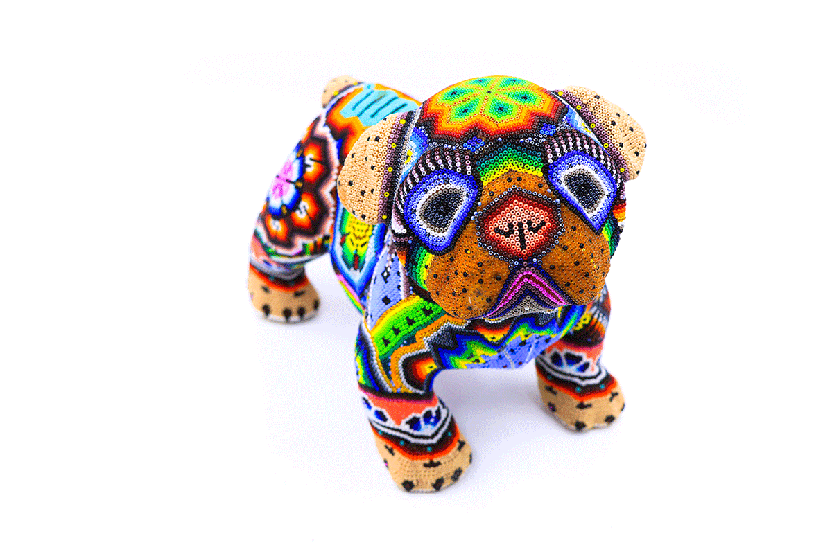 Pequeña escultura de un bulldog en estilo huichol, decorada con chaquira en tonos brillantes y patrones que representan la iconografía wixárika, mostrando la creatividad y la habilidad de los artesanos huicholes