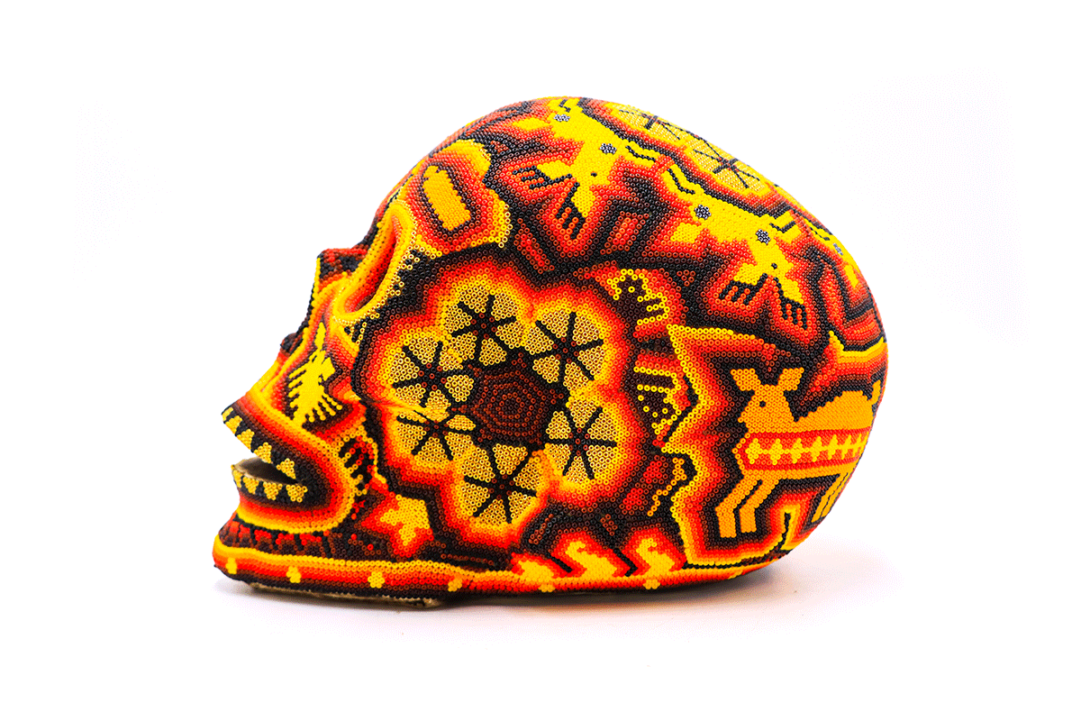 Cráneo grande en estilo huichol con un patrón detallado de chaquiras, mostrando un mosaico de estrellas y formas geométricas en tonos de rojo, amarillo y negro, ofreciendo una visión artística de la iconografía wixárika