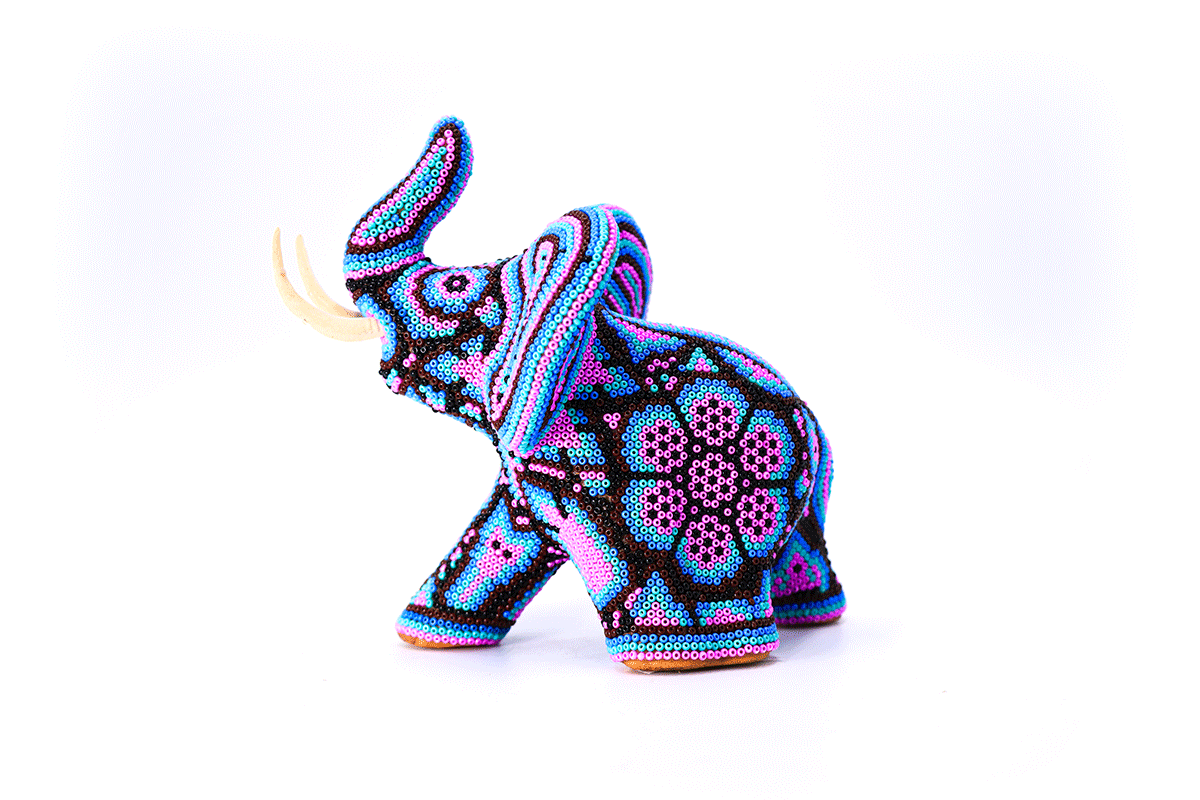 Escultura de elefante Huichol de perfil adornada meticulosamente con cuentas de colores vibrantes formando patrones Wixárika tradicionales, con colmillos prominentes en contraste