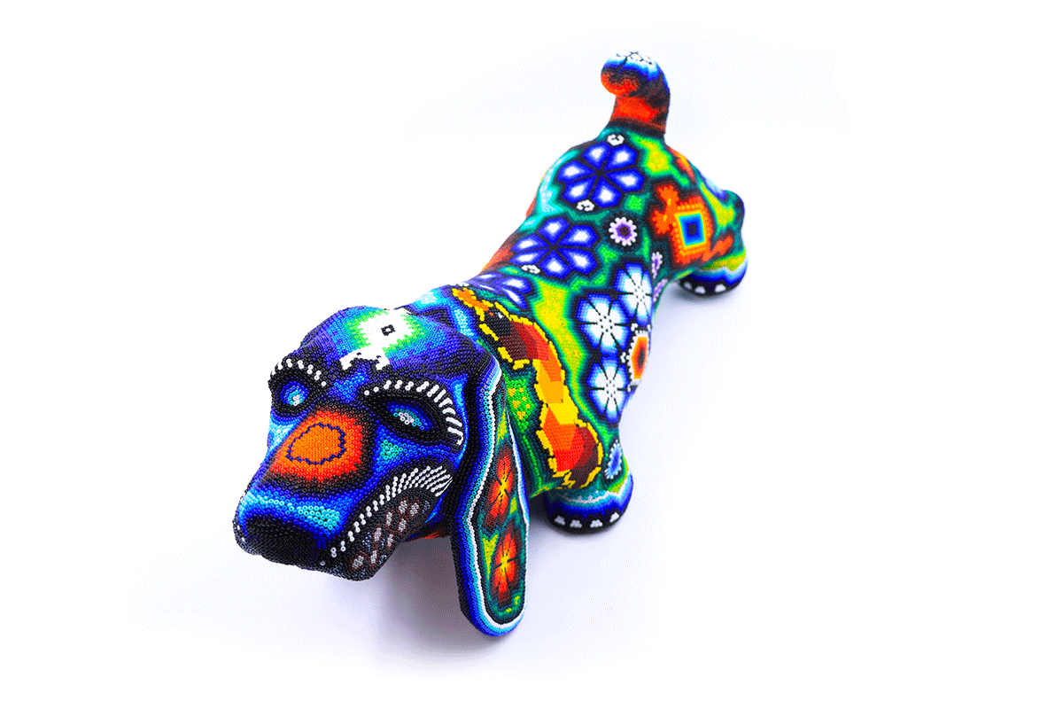 Figura artesanal de perro salchicha con diseño Huichol, mostrando una paleta de colores intensos y motivos tradicionales Wixaritari