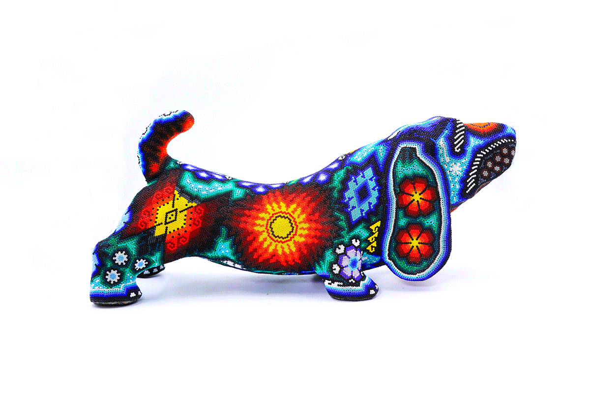 Obra de arte Huichol representando un perro salchicha, con un intrincado trabajo de cuentas en una gama de colores psicodélicos y formas geométricas.