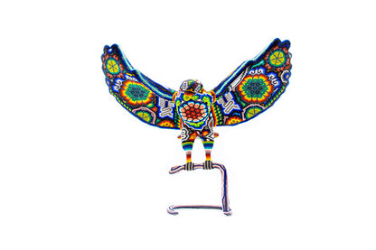 Figura artesanal de águila con alas extendidas, elaborada con cuentas de colores vivos siguiendo patrones tradicionales Huichol, mostrando una serpiente en su pico, sobre un fondo blanco