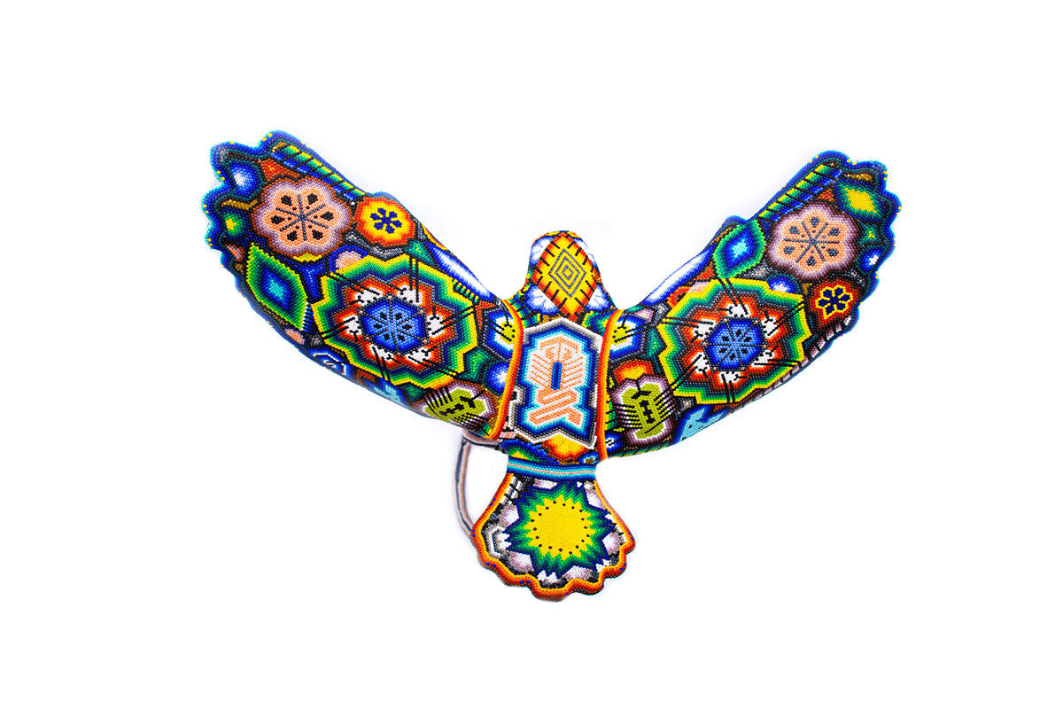 Escultura de águila hecha a mano con cuentas multicolores, con diseño Huichol en las alas extendidas y cuerpo, capturando una serpiente, vista desde arriba, sobre fondo blanco