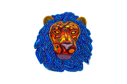 Cabeza de león artesanal elaborada con la técnica de chaquira, destacando en una paleta de colores que combina tonos cálidos de rojo, amarillo y naranja en el rostro, con una exuberante melena en azul profundo y patrones geométricos, evocando el arte tradicional Huichol