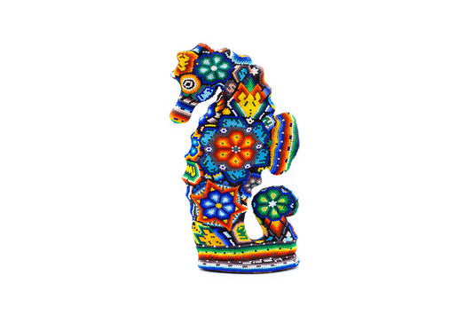 Estatuilla artesanal de un caballito de mar vista de frente, con adornos detallados de cuentas coloridas formando diseños geométricos y florales, resaltando en azul, naranja y verde, contra un fondo blanco