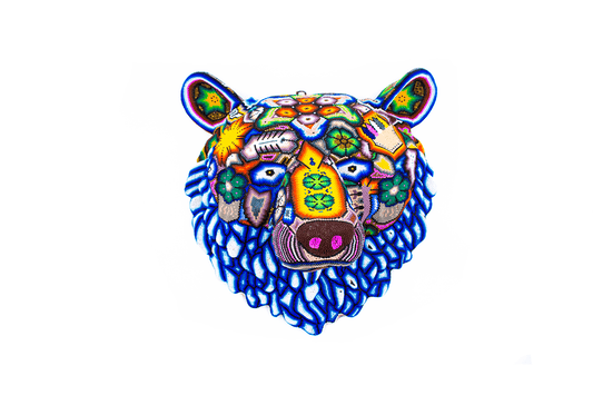 Artesanía de la cabeza de un oso en chaquira, con un complejo patrón de arte Huichol. Los colores primarios son azules y morados, con acentos de otras tonalidades vivas y símbolos tradicionales que decoran el rostro y las orejas del animal
