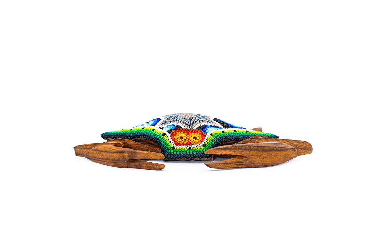 Escultura de cangrejo vista desde arriba, con un diseño intrincado en chaquiras multicolores formando un motivo central estrella, sobre una base de madera y fondo claro