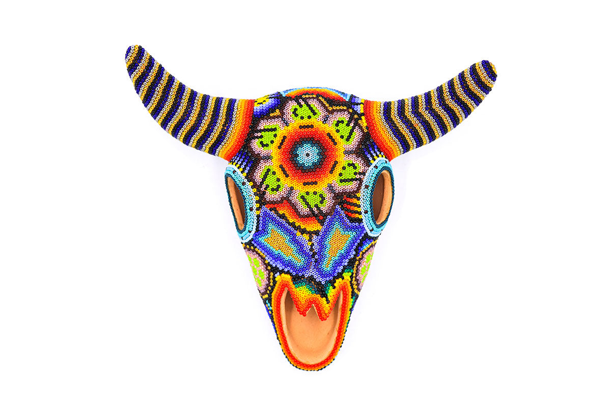 Vista superior de un cráneo de vaca artesanal Huichol, adornado meticulosamente con un mosaico de cuentas vibrantes formando diseños tradicionales Wixarika, listo para decoración de interiores
