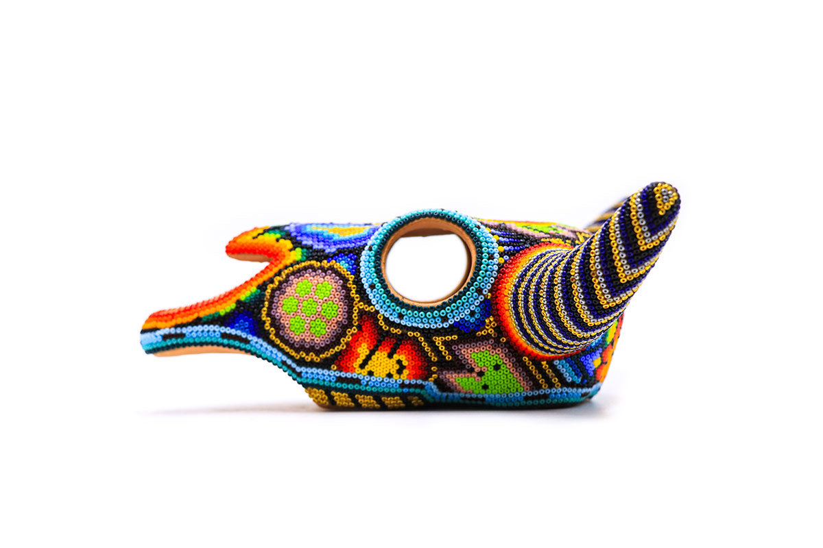 Lateral de una escultura artística Huichol de un cráneo de vaca, con cuentas brillantes formando espirales y formas geométricas coloridas, arte Wixarika contemporáneo