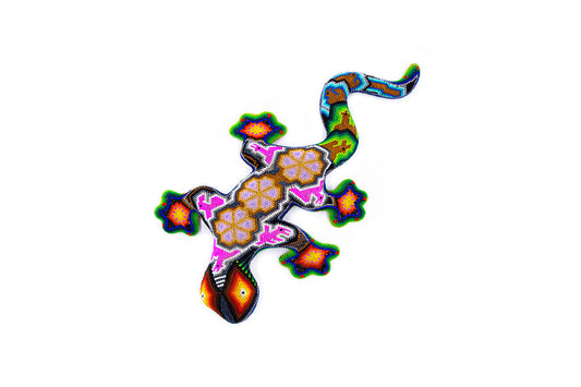 Figura decorativa de un gecko con cuentas de colores, con diseños Huichol que incluyen patrones geométricos y florales en tonos vivos de naranja, verde y azul, resaltados sobre un fondo blanco