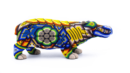 Artisanal beaded hippopotamus sculpture presented in profile view, showcasing rich hues of yellow, blue, and red with intricate Huichol-inspired designs and geometric patterns, set against a white backdrop for contrast