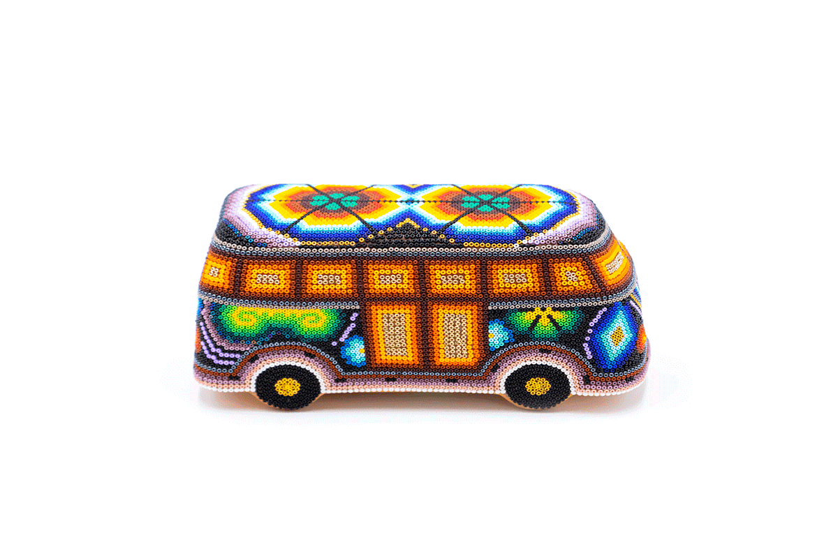 Escultura artesanal en forma de camioneta combi volkswagen, completamente cubierta por un detallado trabajo de chaquiras de colores. Muestra patrones geométricos en tonalidades vibrantes de naranja, azul y verde sobre un fondo blanco
