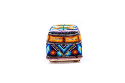 Figura decorativa de una camioneta estilo 'hippie van', adornada con cuentas de colores que forman diseños geométricos y símbolos tribales, con colores llamativos como azul, naranja y violeta, presentada sobre un fondo blanco