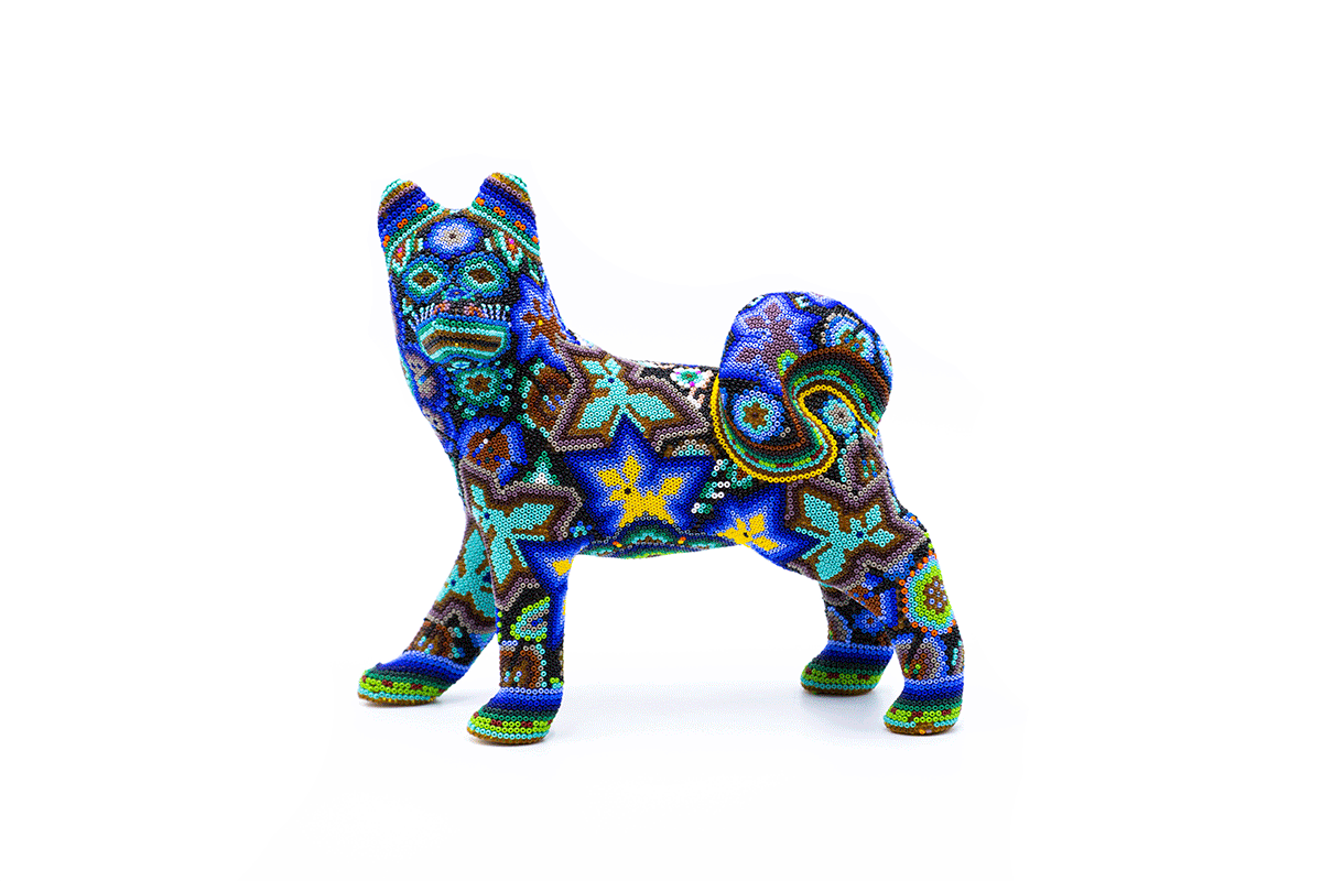 Escultura de un perro husky en posición erguida, con un vibrante mosaico de chaquiras que ilustran patrones geométricos y diseños espirales, destacando tonos de azul, verde y naranja sobre un fondo blanco.