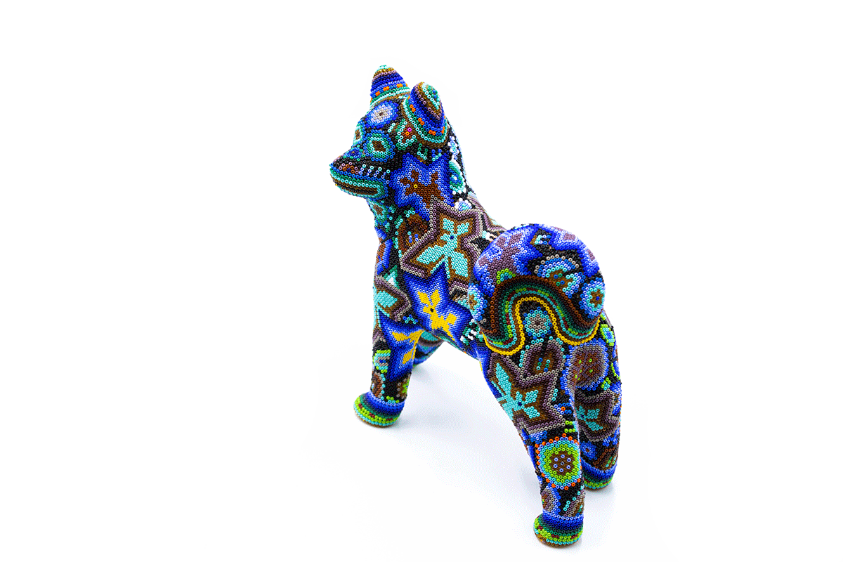 Figura artesanal de un perro husky, meticulosamente decorado con chaquiras coloridas que crean patrones tribales y detalles en espiral, presentando una paleta de colores vivos como azul, naranja y púrpura, en un fondo blanco