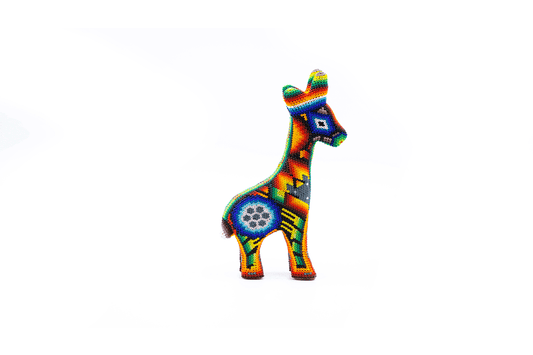 Arte huichol en forma de jirafa pequeña, meticulosamente decorada con cuentas de colores vivos formando patrones tradicionales como estrellas y flores, sobre un fondo blanco.