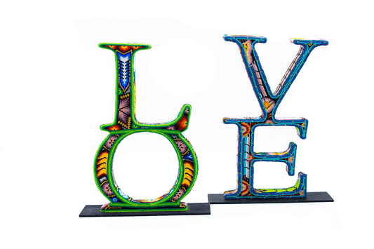 Escultura de las letras 'LOVE' con un diseño tridimensional, elaboradas en técnica de chaquira, presentando una variedad de colores brillantes y patrones detallados inspirados en el arte Huichol, sobre una base negra y contra un fondo blanco