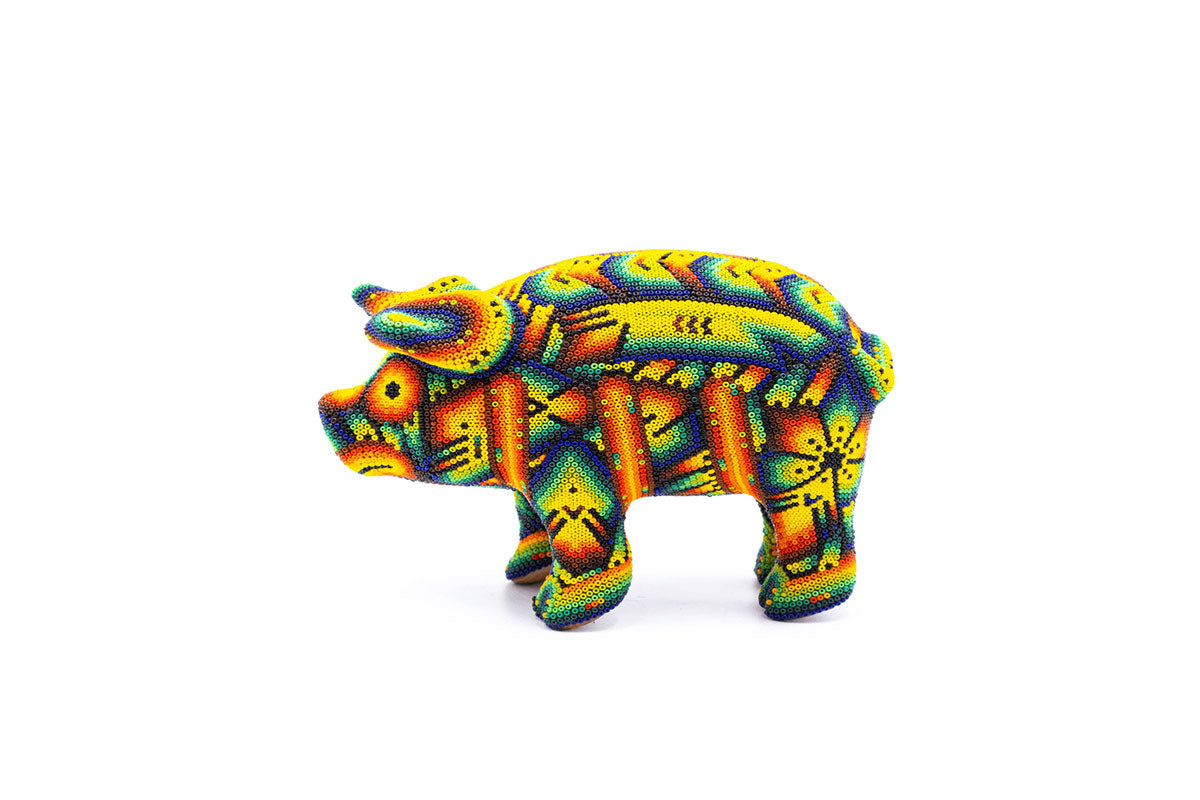 Figura artesanal de un cerdo, detalladamente decorada con patrones de arte huichol en colores vibrantes como amarillo, naranja, rojo, azul y verde. La figura está hecha con técnicas de chaquira, mostrando diseños complejos y simétricos que incluyen formas de flores y espirales.