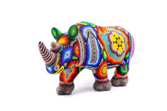 Estatuilla de rinoceronte Huichol decorada con cuentas, mostrando un mosaico de colores vibrantes y patrones étnicos sobre un fondo blanco, arte Wixarika tradicional