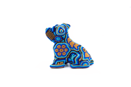 Figura artesanal de un Schnauzer en miniatura, cubierta en chaquiras de colores azules y naranjas con patrones detallados Huichol, en una pose vigilante sobre fondo blanco