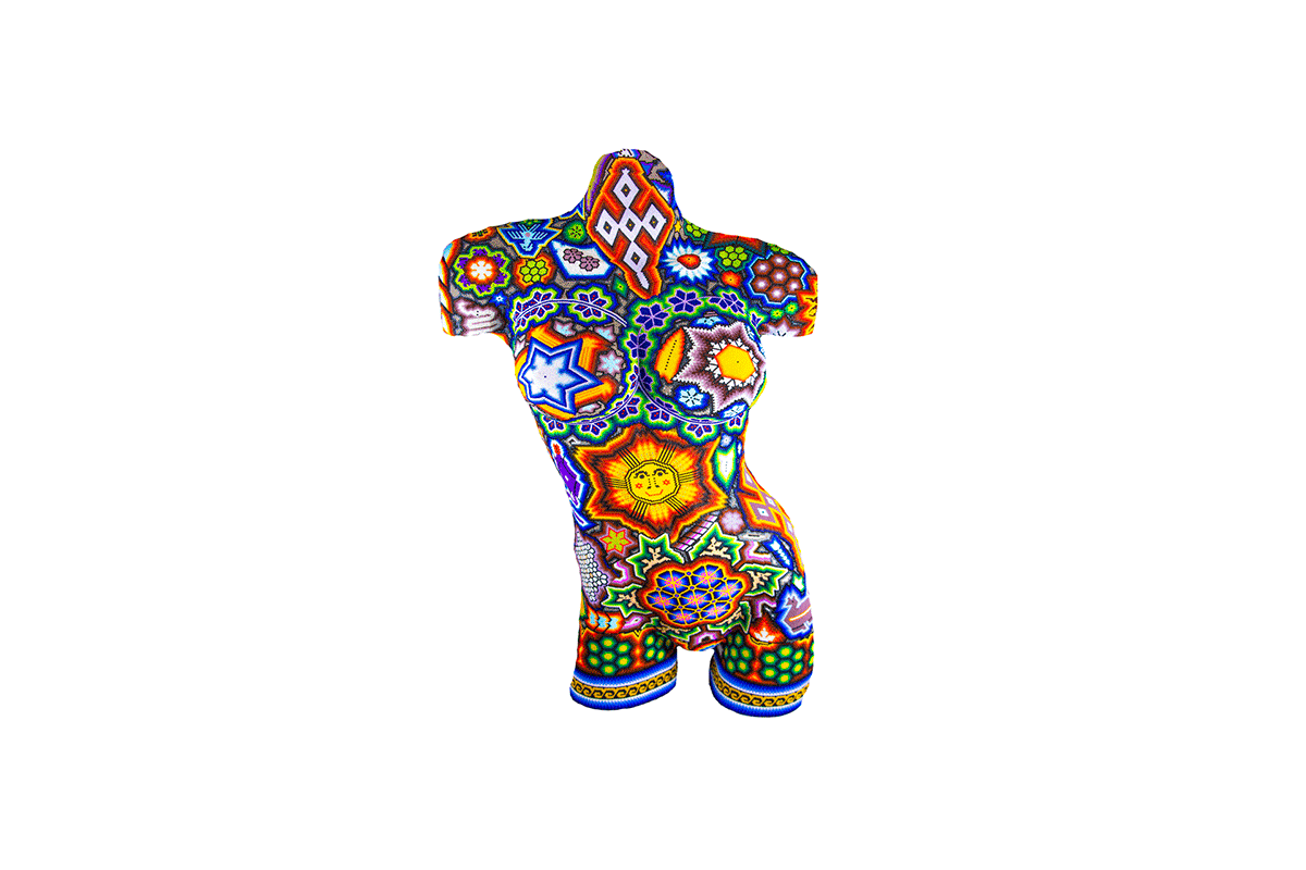 Escultura de un torso de mujer vista de frente, cubierta con un mosaico de chaquira que muestra una explosión de colores y patrones tradicionales Huichol. La pieza artística combina simetría y arte folclórico en una presentación moderna y vibrante