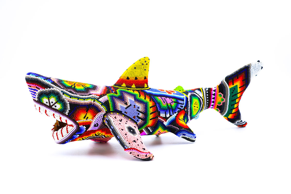 Artesanía Huichol vibrante y colorida en forma de tiburón, meticulosamente decorada con patrones de cuentas brillantes que representan la rica cultura Wixárika