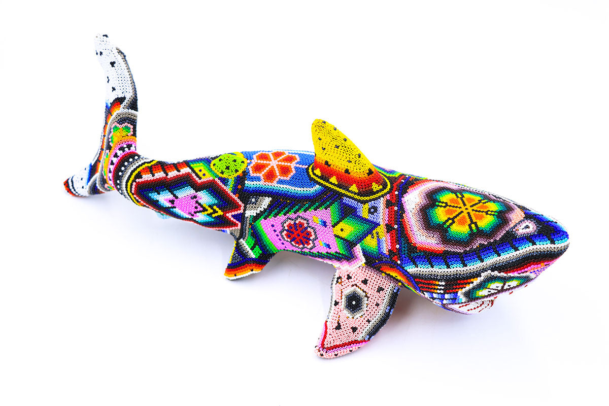 Escultura Huichol de un tiburón, elaborada con una técnica de chaquira, exhibiendo motivos geométricos y simbología Wixárika que celebra la espiritualidad y la naturaleza