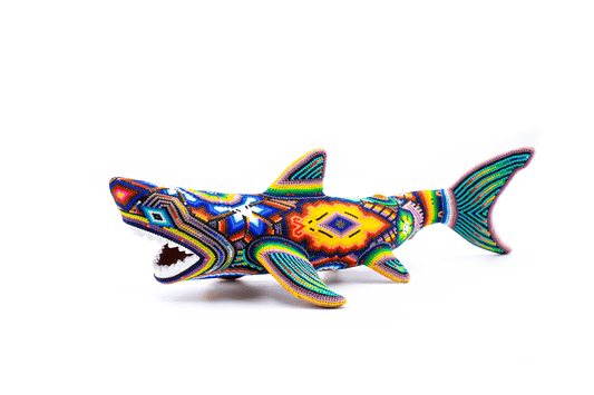 Figura decorativa de tiburón blanco con la boca abierta perfil izquierdo, mostrando un intrincado trabajo de chaquiras que crean efectos visuales vibrantes y detallados, en una paleta de colores que va desde el azul profundo hasta el naranja brillante, en un fondo blanco