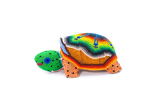 Figura artesanal de una tortuga de tierra con un caparazón de vivos colores y cuentas dispuestas en complejos patrones Huichol, destacando sobre un fondo blanco