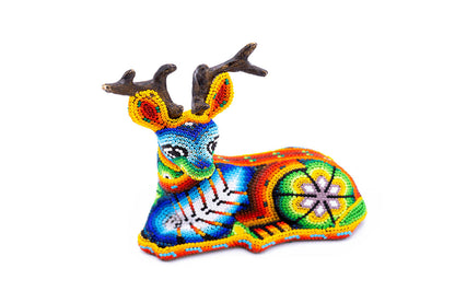 Artesanía de venado en chaquiras, con diseño detallado Huichol en perspectiva lateral, destacando una paleta de colores vivos y formas geométricas, contra un fondo blanco puro