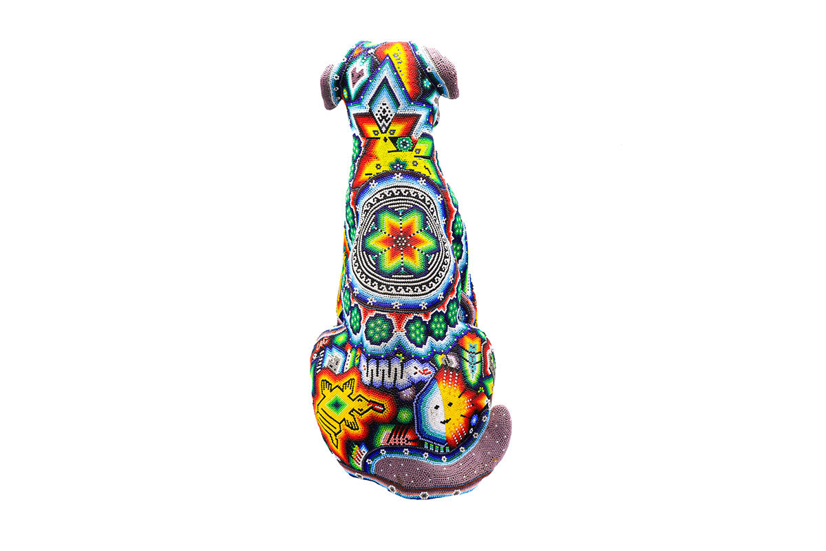 Escultura de perro Schnauzer Huichol vista desde atrás, mostrando patrones geométricos y simbología Wixárika en una paleta de colores intenso